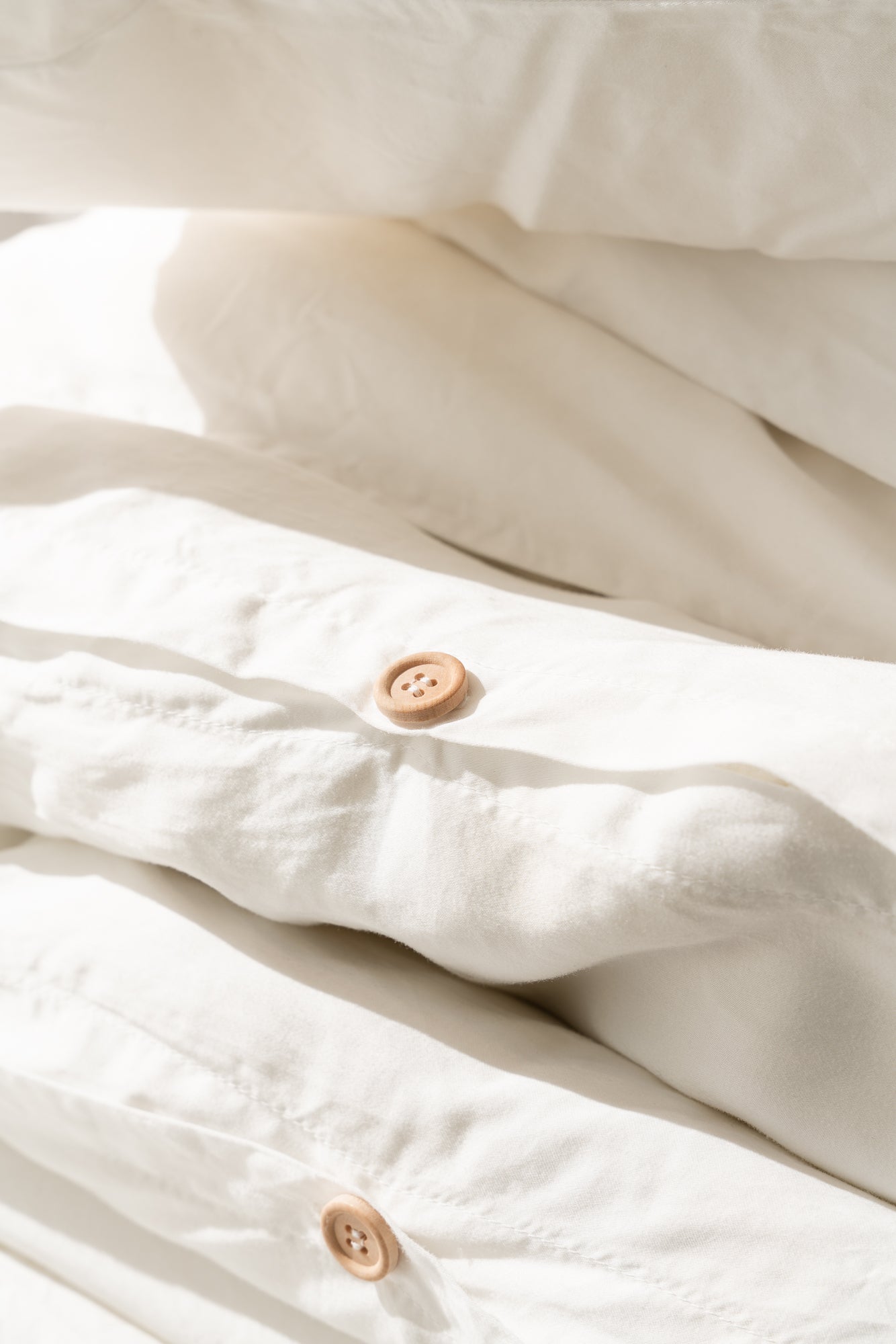 Stack of white bedding with bamboo buttons on a light background
