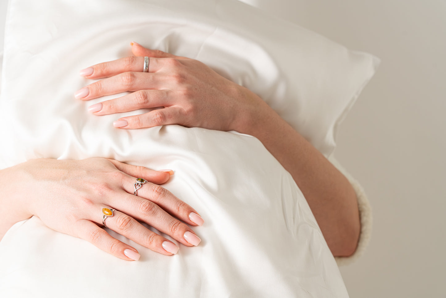 Close-up of hands with rings on a white pillow